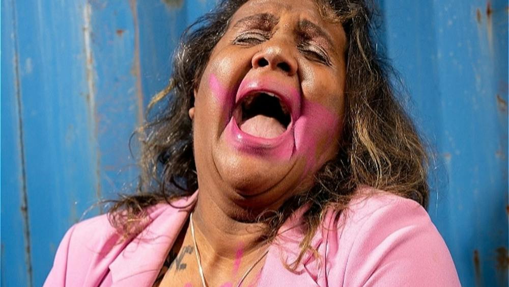 A First Nations woman in a pink blazer with makeup smeared and looking to be crying