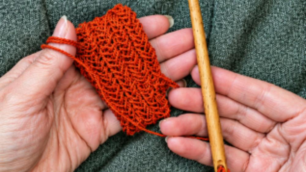 Pair of hands holding knitted yarn in one and a needle in the other