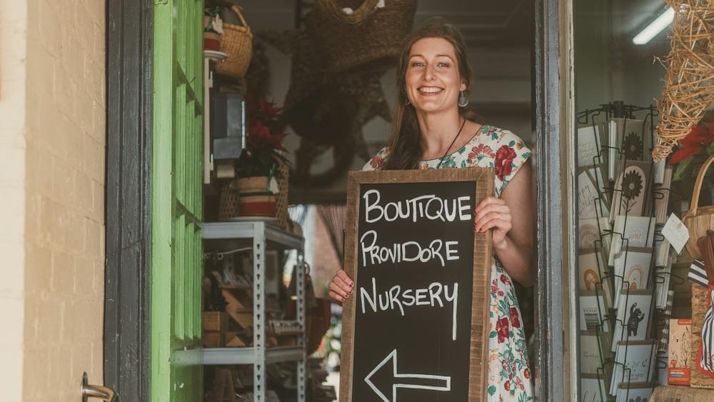 woman holding sign that says, boutique, providore, nursery