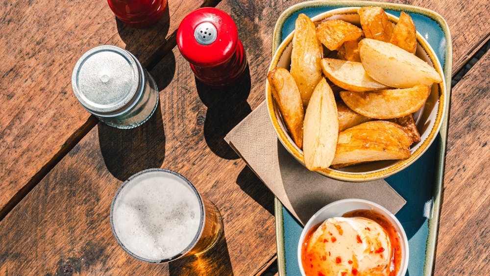Above view image of hand cut potato wedges with condiments and drinks