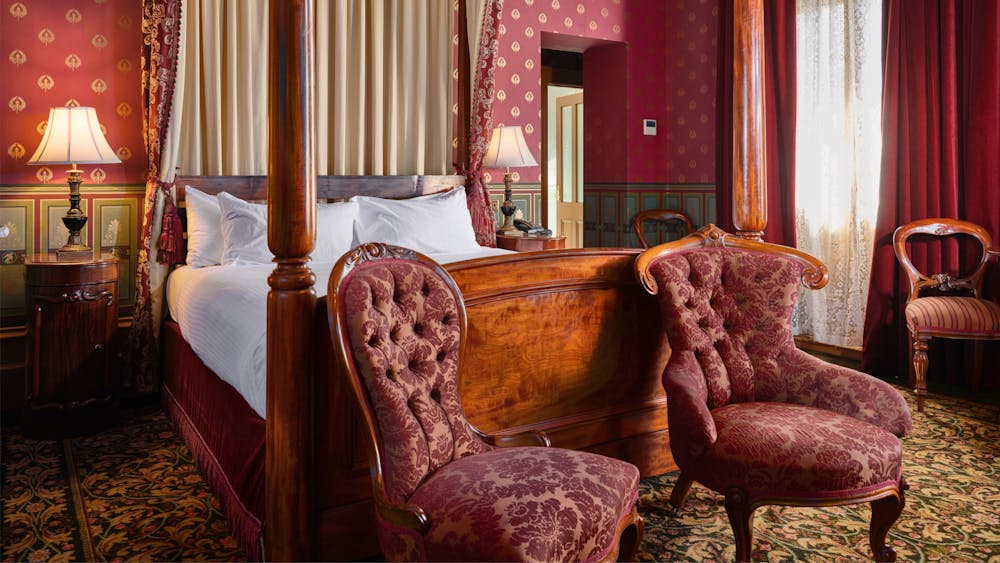 Bedroom with red wallpaper, bed, bedside table and vintage looking chairs