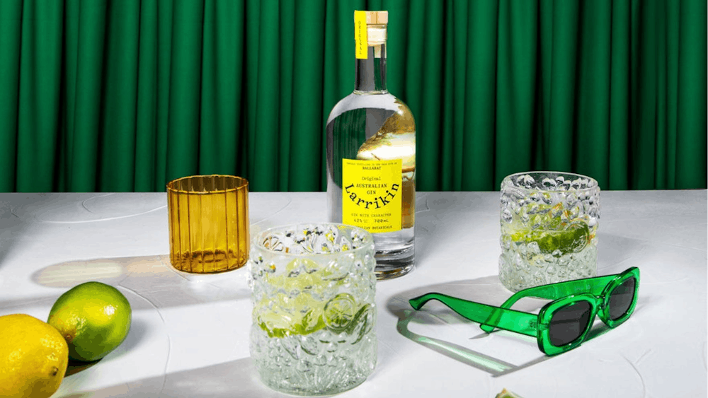 A table with a bottle of gin, sunglasses, two glasses and some lemons and limes