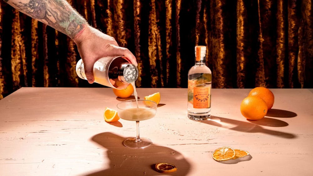 A mad with a tattooed arm pouring gin into a glass