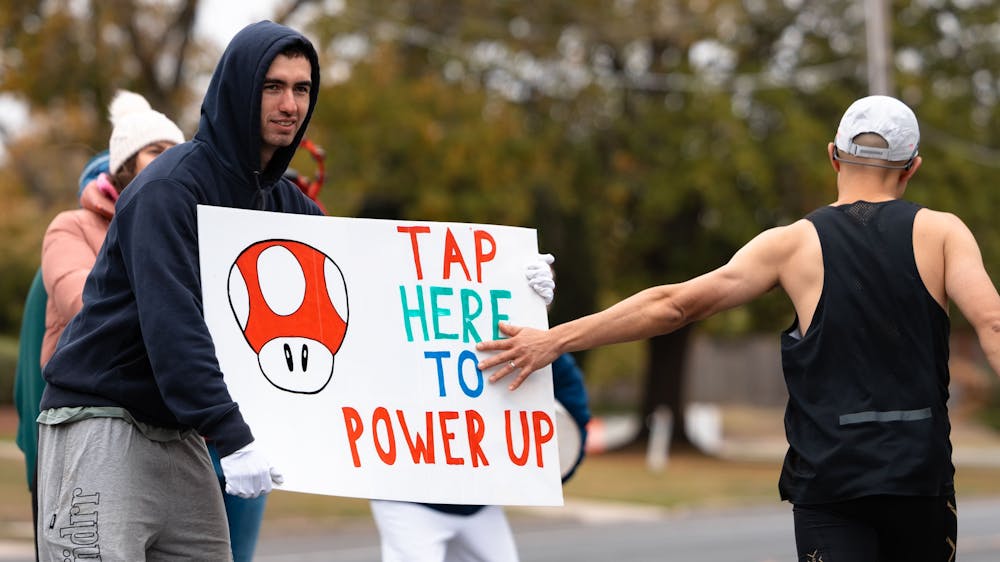 A male runner taps a sign being held by a spectator in Victoria Park, Ballarat