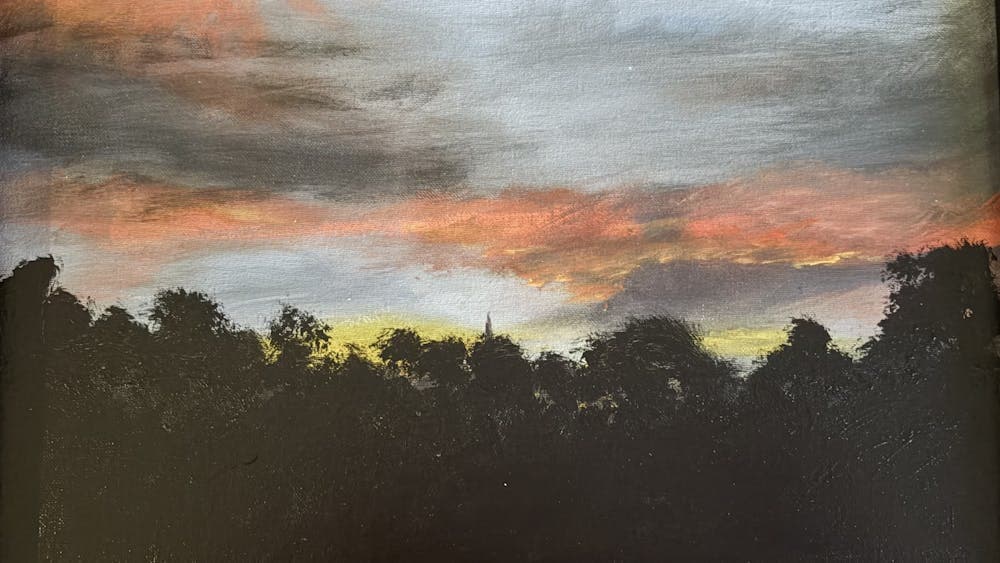 A dark silhouette of trees with a colourful orange blue yellow and grey clouded sky above