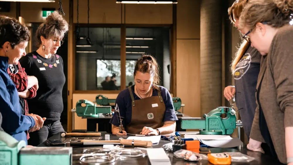 Instructor seated at bench showing participants how to make jewellery