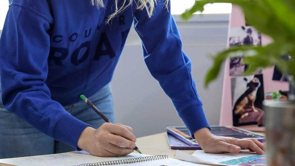 Artist Jenna Oldaker standing while sketching art in blue jumper