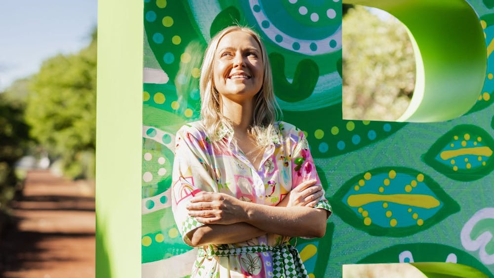 Indigenous artist Jenna Oldaker standing in front of her Begonia Festival artwork