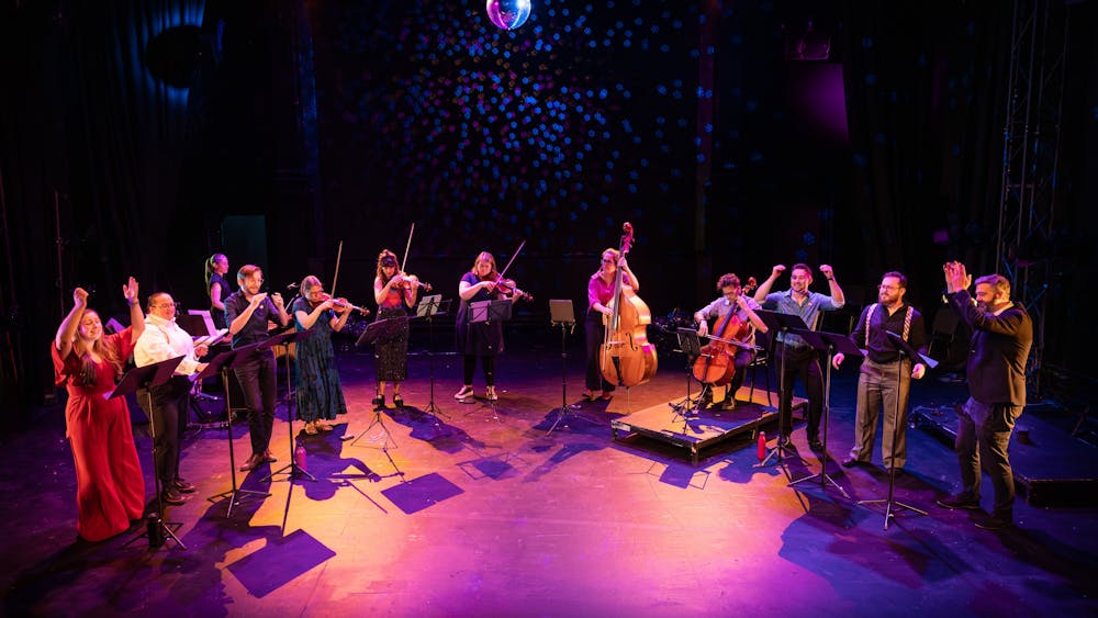Singers and string players stand and perform under a disco ball