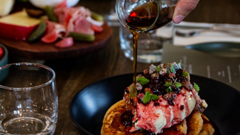 Maple syrup poured over pancakes topped with berries and mascarpone cream.