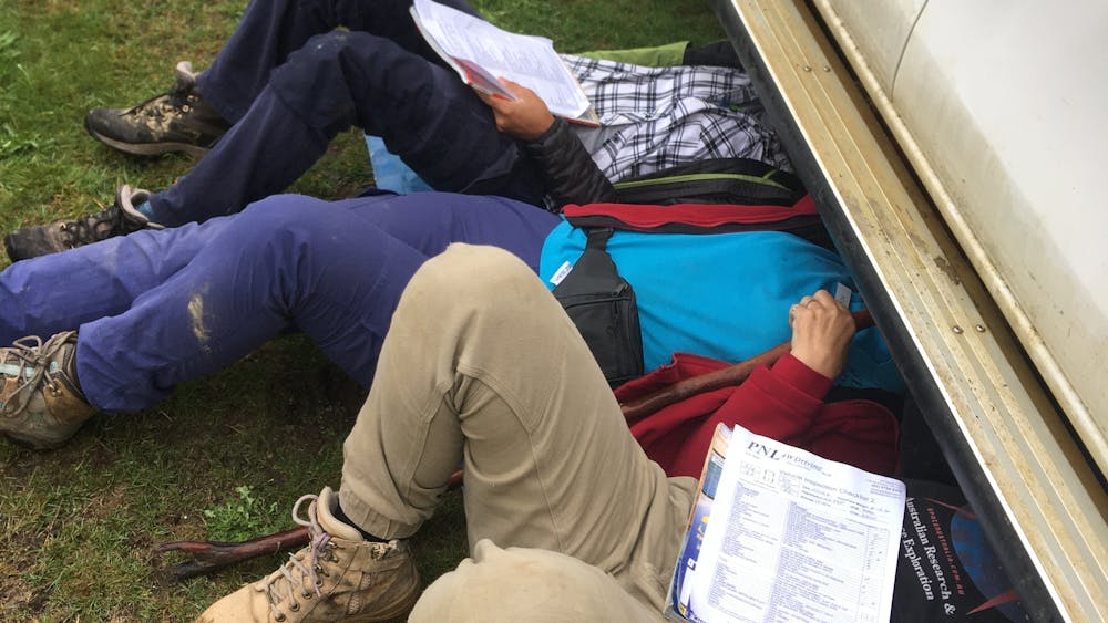 A instructor lays on the ground, looking underneath a car with two people by their side.