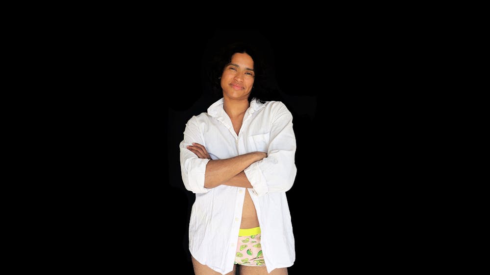 Neptune faces the camera, arms folded, smiling warmly, wearing a white shirt and underwear