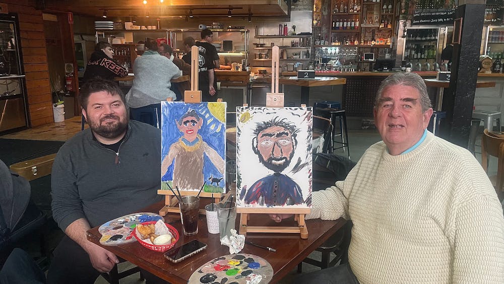 2 people are holding paintings done by each other