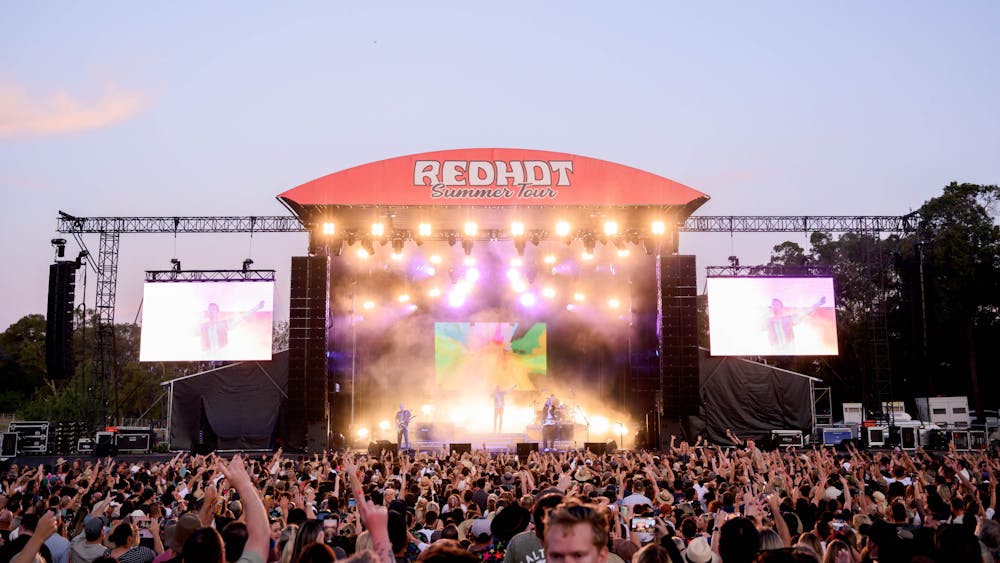 Crowd at a festival in front of a stage at sunset.