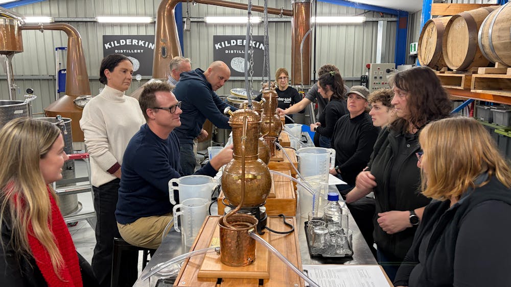 Ten adults sitting at bench with small stills distilling gin